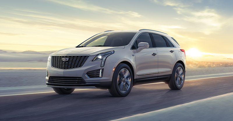 A white 2025 Cadillac XT5 driving down the highway while the sun rises
