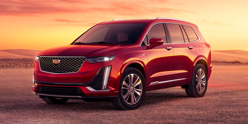 Front driver's side view of a red 2025 Cadillac XT6 parked on a beach at dusk