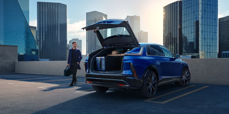 Cadillac Lyriq electric SUV with open trunk in a city parking lot at sunset
