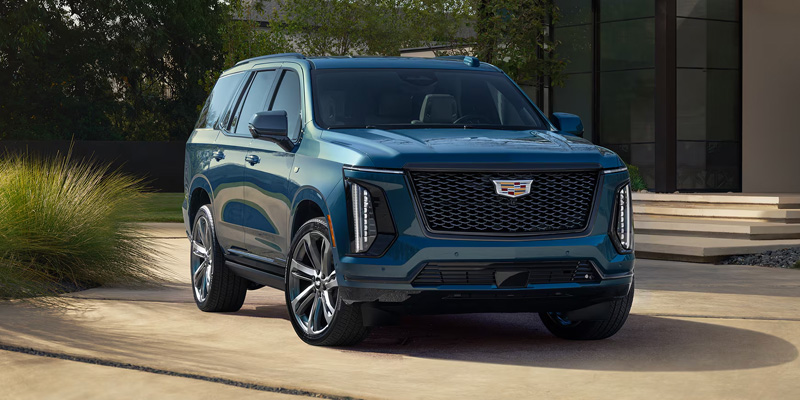 Blue Cadillac SUV parked in a modern driveway surrounded by greenery.