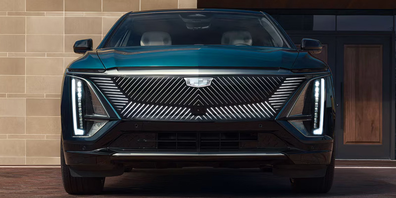 Front view of a black Cadillac LYRIQ with illuminated vertical headlights and a patterned grille.