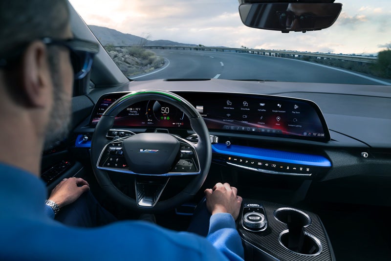 Front View of the 2026 OPTIQ-V Driving Through the Dusk Utilizing its Headlights | Cadillac of Portland in portland OR