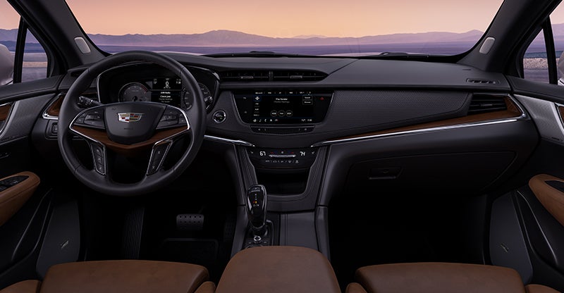Cadillac SUV interior showing steering wheel, dashboard, and center console in a wide cockpit view.