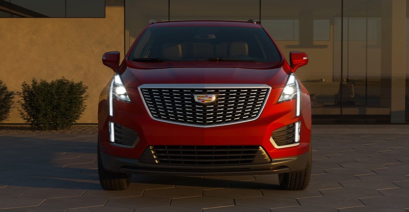Front view of red Cadillac SUV with illuminated headlights.