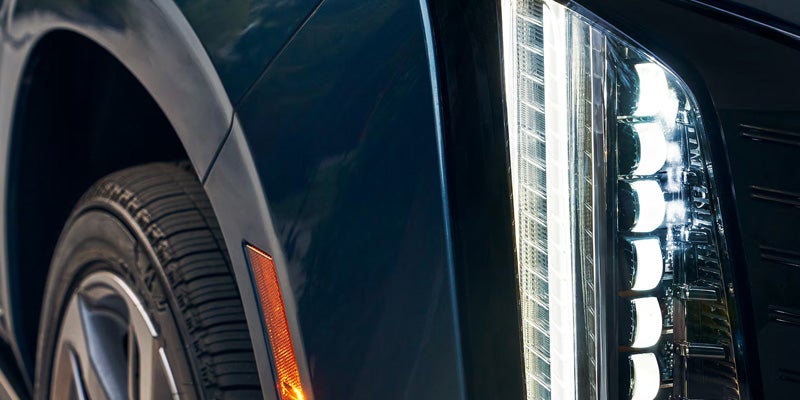 Close-up of the 2026 Cadillac Escalade's headlight, tire, and powertrain, showcasing its detailed design.