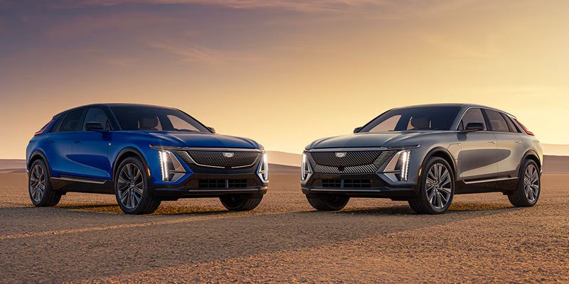 Two Cadillac SUVs parked side by side on a desert road at sunset.